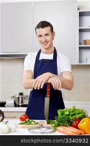 The young man in an apron with a knife at kitchen
