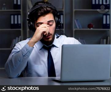 The young man in call center concept working late overtime in office. Young man in call center concept working late overtime in office