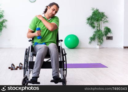 The young man in wheel-chair doing exercises indoors. Young man in wheel-chair doing exercises indoors