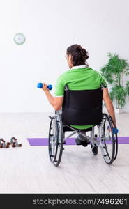 The young man in wheel-chair doing exercises indoors. Young man in wheel-chair doing exercises indoors