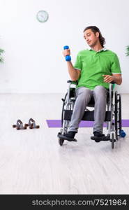 The young man in wheel-chair doing exercises indoors. Young man in wheel-chair doing exercises indoors