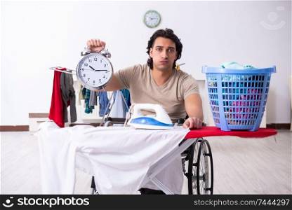 The young man in wheel-chair doing ironing at home . Young man in wheel-chair doing ironing at home 