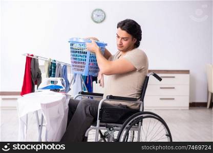 The young man in wheel-chair doing ironing at home . Young man in wheel-chair doing ironing at home 