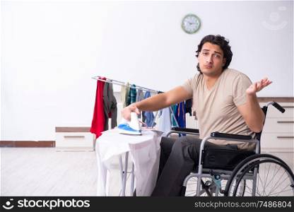 The young man in wheel-chair doing ironing at home . Young man in wheel-chair doing ironing at home