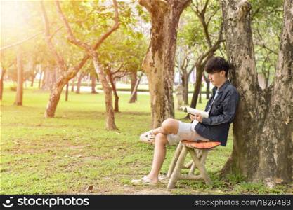 The young man is sitting and relaxing, reading a book in the park.