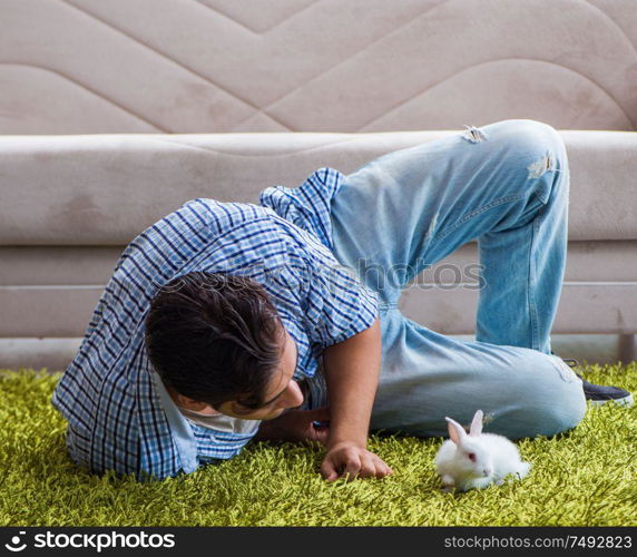 The young man playing with pet rabbit at home. Young man playing with pet rabbit at home