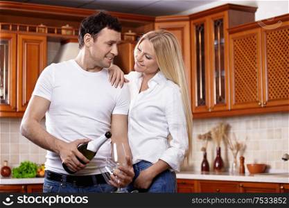 The young man pours champagne in glasses with the girl on kitchen