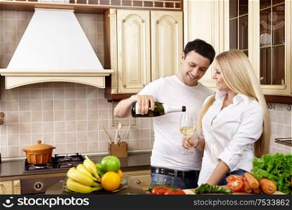 The young man pours champagne to the girl on kitchen