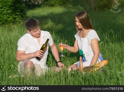 The young man pours to girl a white wine in a glass during a picnic in a city park