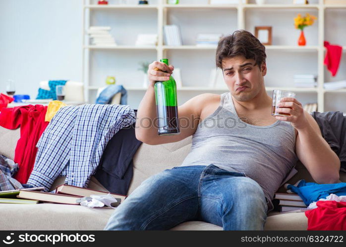 The young man student drunk drinking alcohol in a messy room. Young man student drunk drinking alcohol in a messy room