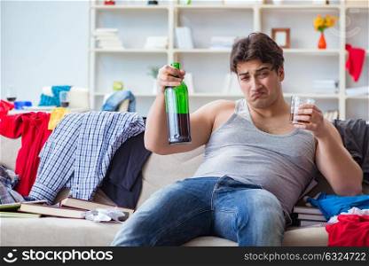 The young man student drunk drinking alcohol in a messy room. Young man student drunk drinking alcohol in a messy room