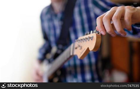 The young man tuning the electric guitar. Closeup