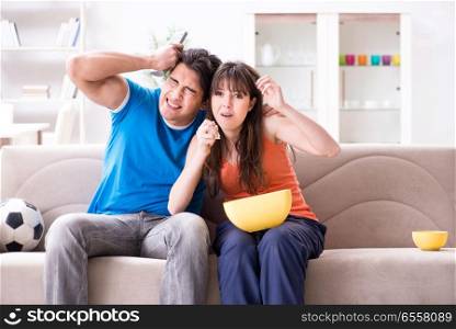 The young man watching football with his wife at home. Young man watching football with his wife at home. The young man watching football with his wife at home