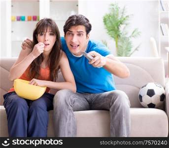 The young man watching football with his wife at home. Young man watching football with his wife at home