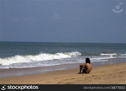 The young man with long hair sits on the coast and looks at the sea. India Goa.. The young man with long hair sits on the coast and looks at the sea. India Goa