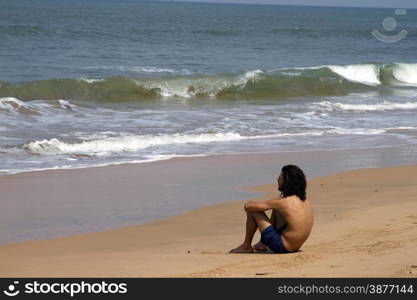 The young man with long hair sits on the coast and looks at the sea. India Goa.. The young man with long hair sits on the coast and looks at the sea. India Goa