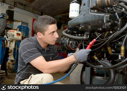 The young mechanic cleans the engine with compressed air
