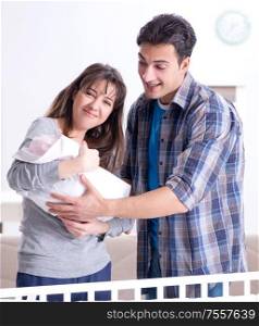 The young parents with their newborn baby near bed cot. Young parents with their newborn baby near bed cot