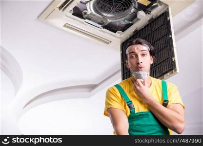 The young repairman repairing ceiling air conditioning unit . Young repairman repairing ceiling air conditioning unit