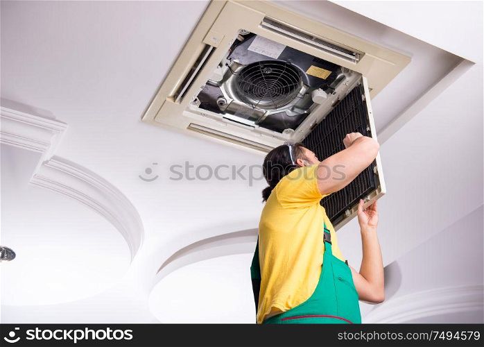 The young repairman repairing ceiling air conditioning unit. Young repairman repairing ceiling air conditioning unit