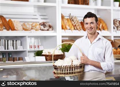 The young seller holds a basket with cakes in shop