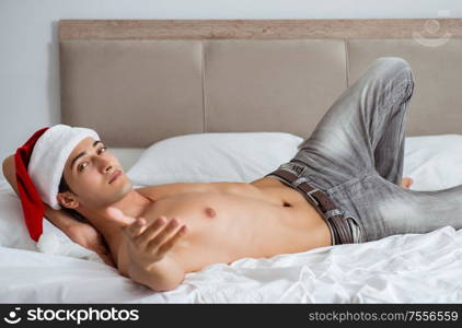 The young sexy man wearing santa hat in bed. Young sexy man wearing santa hat in bed