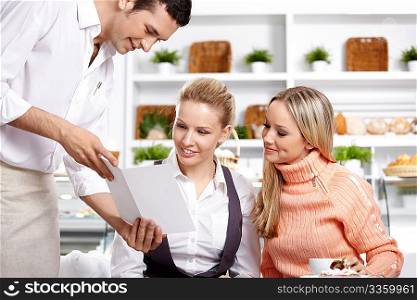 The young waiter shows the menu to two girls