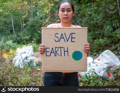 "The young woman holding "Save The Earth" Poster showing a sign protesting against plastic pollution in the forest. The concept of World Environment Day. Zero waste."