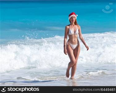 The young woman in a hat of Santa Claus goes on a beach at sea edge