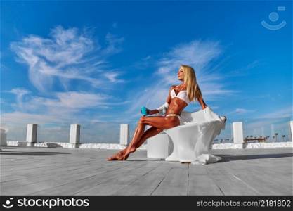 The young woman in white pareo on a terrace and blue sky on a background.. The young woman in white pareo on a terrace and blue sky on a background