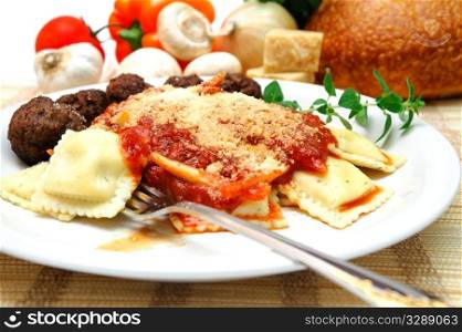 Thee cheese ravioli with parmesean cheese sprinkled on top, small meatballs on the side. Fresh vegetables, cheese and bread in the background.. Ravioli And Meatballs