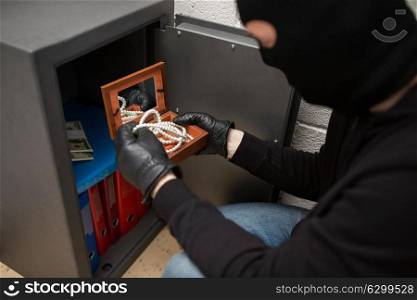 theft, burglary and people concept - thief in mask stealing valuables from safe at crime scene. thief stealing valuables from safe at crime scene