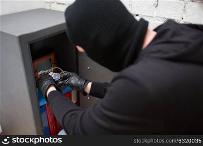 theft, burglary and people concept - thief in mask stealing valuables from safe at crime scene. thief stealing valuables from safe at crime scene