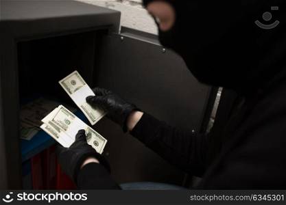 theft, burglary and people concept - thief stealing money from safe at crime scene (staged photo). thief stealing money from safe at crime scene