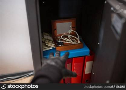 theft, burglary and people concept - thief stealing valuables from safe at crime scene. thief stealing valuables from safe at crime scene