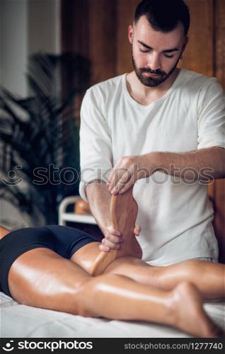 Therapist doing anti cellulite Madero therapy massage to attractive sporty young woman, lying on white towel, wooden background