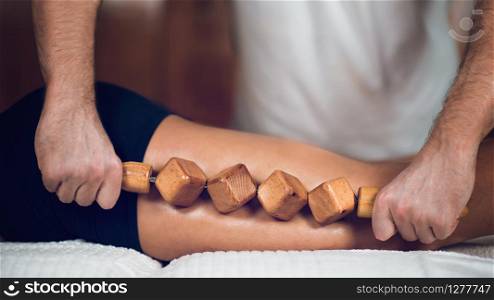 Therapist doing anti cellulite Madero therapy massage to attractive sporty young woman, lying on white towel, wooden background