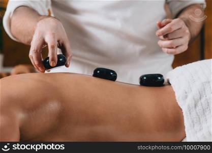 Therapist doing hot stone massage young attractive woman lying on massage table
