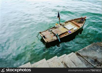 There is a small boat parking at a concrete dock, the boat looks old and messy with old paint cans and steering wheel
