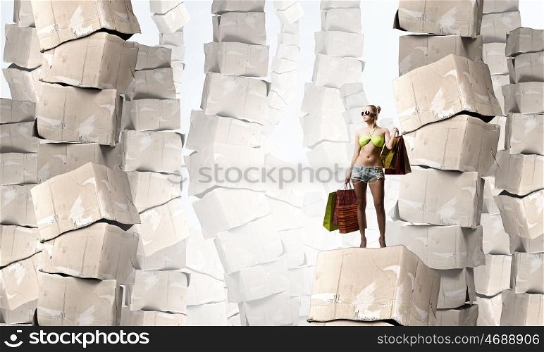 There is never too much shopping. Beautiful young girl in bikini with shopping bags on pile of carton boxes