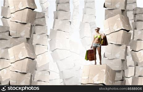 There is never too much shopping. Beautiful young girl in bikini with shopping bags on pile of carton boxes