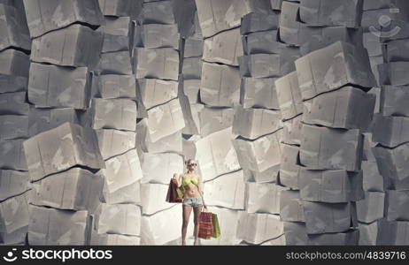 There is never too much shopping. Beautiful young girl in bikini with shopping bags on pile of carton boxes