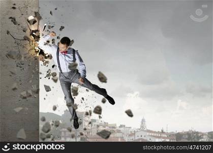 There is no barriers for him. Emotional businessman breaking stone wall with karate punch