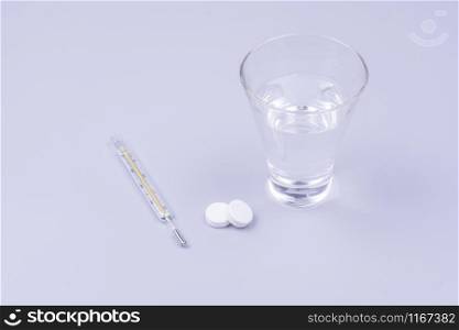 thermometer, glass of water and pills, objects on gray background, top view. thermometer pills and a glass of water