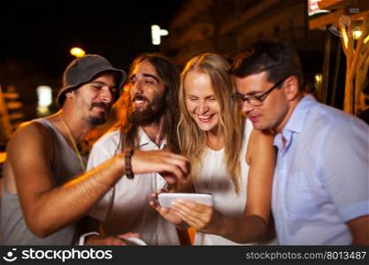 They looking through nice shots on mobile. Young happy friends outdoor at night. They look at photos they made with smart phone. They laughing and getting excited