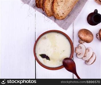 thick creamy soup with mushrooms in a round clay plate on a white wooden background, top view