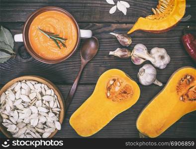 thick pumpkin soup in a ceramic plate and half fresh pumpkin on a brown wooden background, top view