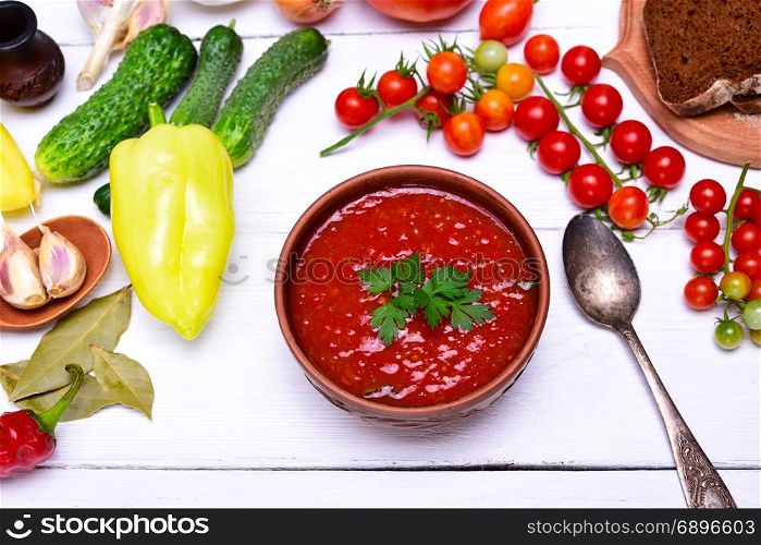 thick soup of tomato and vegetables gazpacho in a brown round plate on a white table