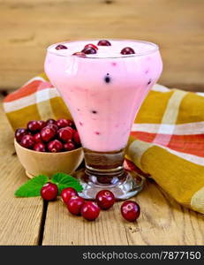 Thick yogurt in a glass goblet with cranberries, napkin, cranberries in a bowl, mint on a wooden boards background