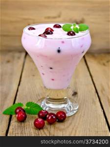 Thick yogurt in glass with cranberries, mint on a wooden boards background